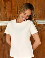 Vue de face du T-shirt écru col rond pour femme en coton, modèle Taiga de la marque LA PETITE ÉTOILE. Présente une coupe droite à manches courtes et un boutonnage aspect corne sur l'épaule gauche.