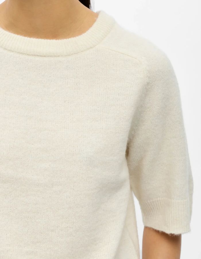 Col du T-shirt en maille fine pour femme de couleur blanc crème écru chiné Birch Melange, modèle Denisi de la marque Object. Présente une coupe droite avec col rond classique et des manches mi-longues arrivant au coude, terminées par de larges bords-côtes élastiques.