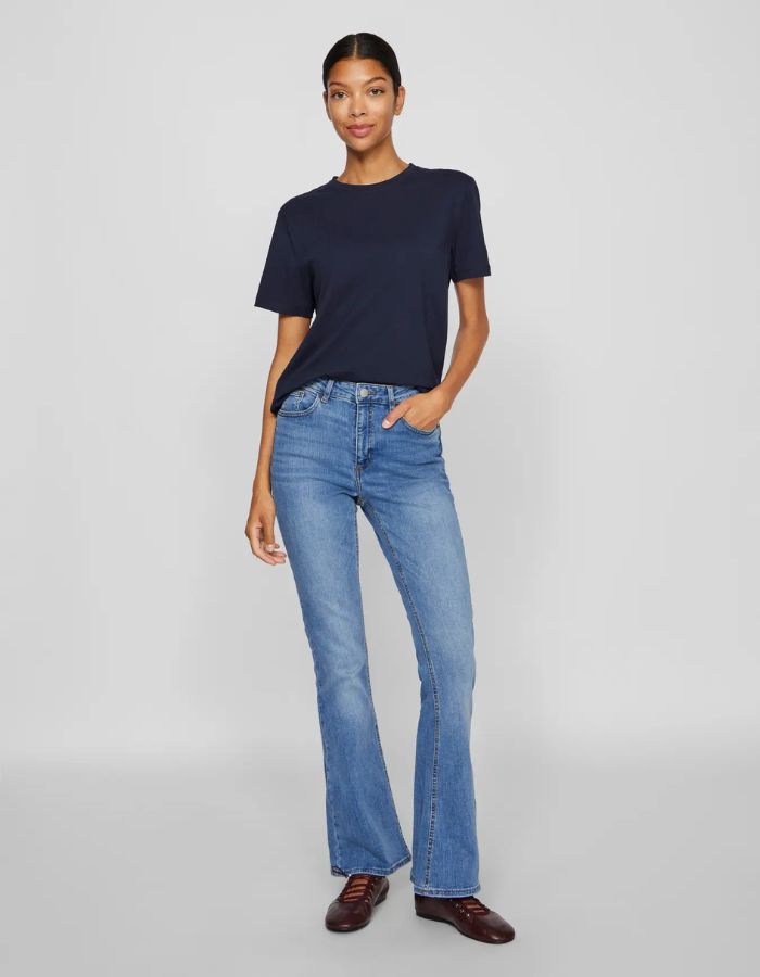 Femme portant un t-shirt navy en coton bio à manches courtes et col rond, avec un jean bleu évasé.