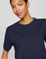 Femme souriante portant un t-shirt Nora Vila bleu marine en jersey de coton biologique, col rond, manches courtes.