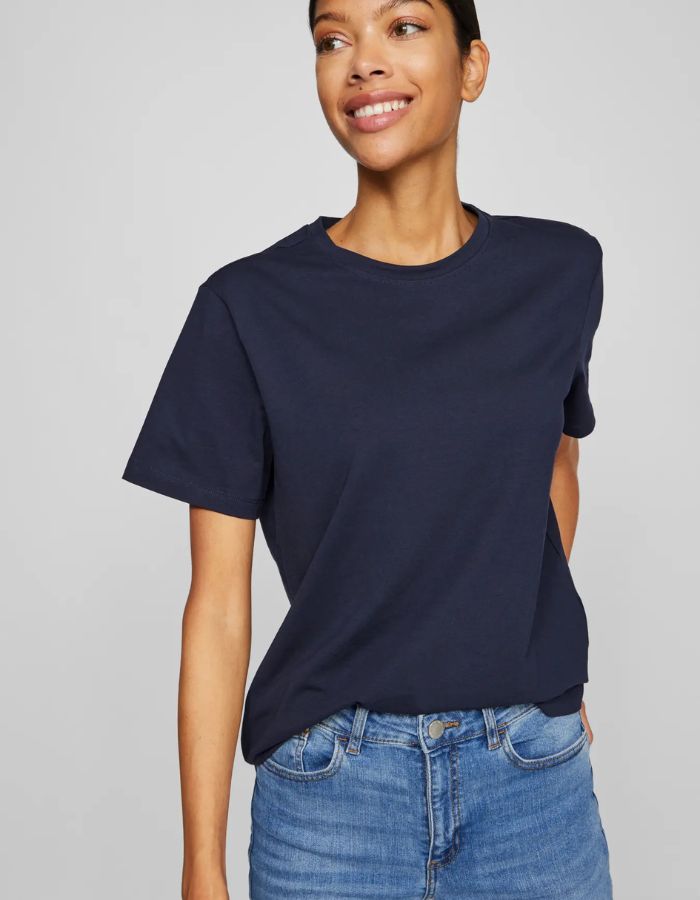 Femme souriante portant un t-shirt Nora Vila bleu marine en jersey de coton biologique, coupe droite.