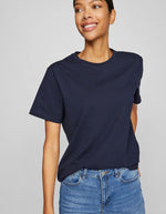 Femme souriante portant un t-shirt Nora Vila bleu marine en jersey de coton biologique, coupe droite.