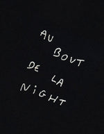 Broderie du T-shirt noir à manches courtes pour homme en coton biologique, modèle Popincourt de la marque Maison Labiche. Présente une coupe droite avec col rond en bord-côte et la phrase 'Au Bout De La Night' brodée en lettres fines sur le côté gauche de la poitrine.