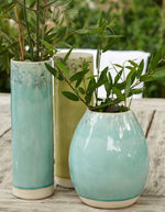 Trois vases en grès faits main, bleu turquoise et vert, avec des plantes vertes, sur une table en bois.
