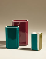 Trois vases Facettes en faïence émaillée: un grand bordeaux, un moyen bleu sarcelle, et un petit bicolore vert olive et bleu sarcelle.