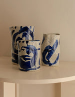 Trio des vases en grès artisanal Sophia par Marie Michielssen, de couleur blanche avec des motifs calligraphiques peints à la main en bleu profond. Silhouette organique asymétrique et design minimaliste de 19 cm de hauteur.