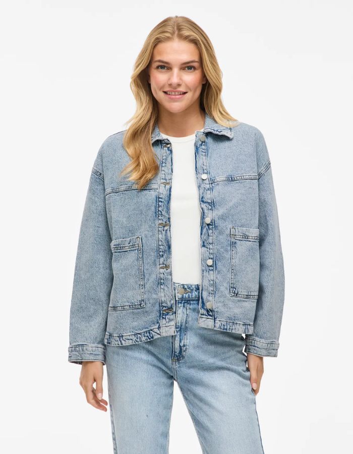 Femme souriante portant une veste en jean bleu clair Jaf avec col chemise, fermeture boutonnée et poches plaquées.