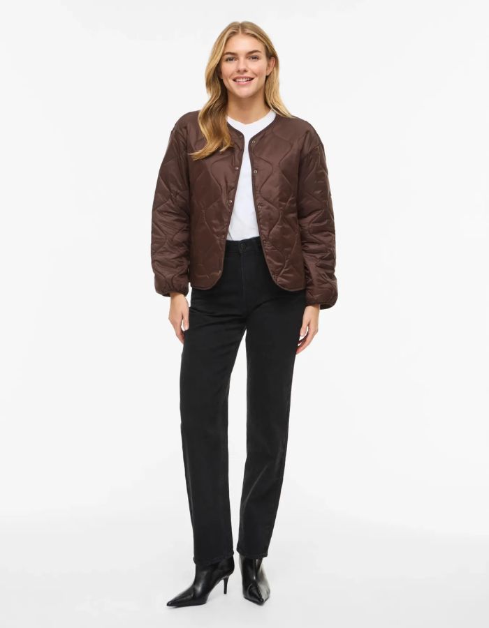 Silhouette avec la Veste matelassée légère et courte pour femme de couleur marron chocolat, modèle Dune de la marque Vila. Présente un col en V, des manches longues, des poches plaquées à l'avant et une fermeture par boutons-pression.