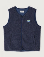 Veste sans manches pour homme de couleur bleu nuit foncé Astre Chiné, modèle Hoktown de la marque American Vintage. Confectionnée dans une matière épaisse effet mouton retourné shearling, elle présente un col montant bas, une fermeture à boutons-pression, deux poches zippées et un patch logo sur la poitrine.