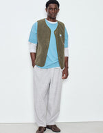 Silhouette avec la Veste sans manches pour homme de couleur vert kaki Varan Chiné, modèle Hoktown de la marque American Vintage. Confectionnée dans une matière épaisse effet mouton retourné shearling, elle présente un col montant bas, une fermeture à boutons-pression, deux poches zippées et un patch logo sur la poitrine.