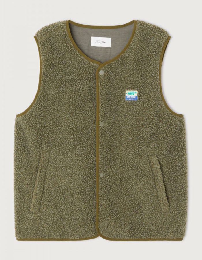 Veste sans manches pour homme de couleur vert kaki Varan Chiné, modèle Hoktown de la marque American Vintage. Confectionnée dans une matière épaisse effet mouton retourné shearling, elle présente un col montant bas, une fermeture à boutons-pression, deux poches zippées et un patch logo sur la poitrine.