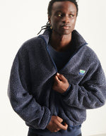 Vue de face de la Veste zippée à manches longues pour homme de couleur bleu nuit foncé Astre Chiné, modèle Hoktown de la marque American Vintage. Confectionnée dans une matière épaisse effet mouton retourné shearling, elle présente un col montant bas, une fermeture éclair, deux poches zippées et un écusson logo AMV sur la poitrine.