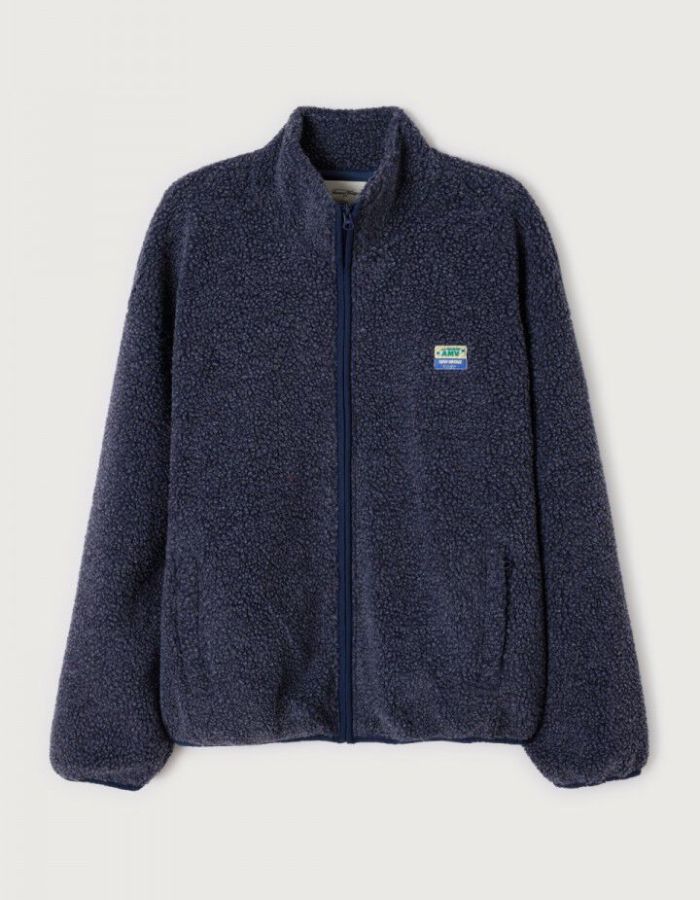 Veste zippée à manches longues pour homme de couleur bleu nuit foncé Astre Chiné, modèle Hoktown de la marque American Vintage. Confectionnée dans une matière épaisse effet mouton retourné shearling, elle présente un col montant bas, une fermeture éclair, deux poches zippées et un écusson logo AMV sur la poitrine.