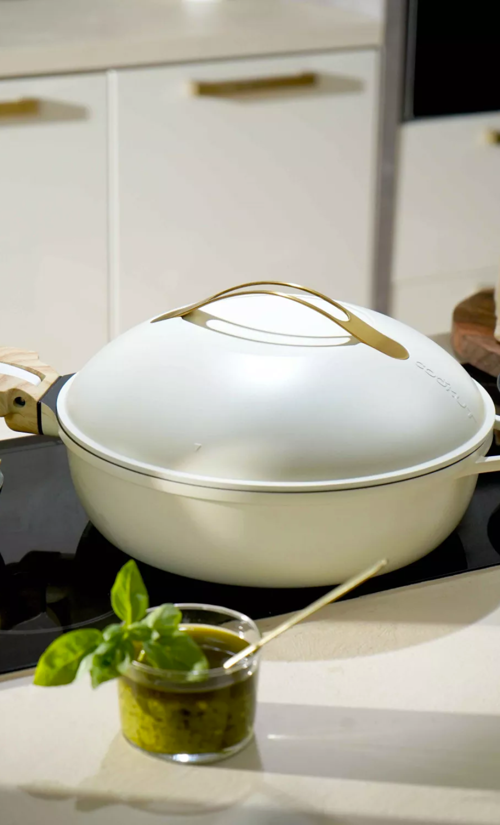 La Fabuleuse Poêle Cookut 28cm blanche avec couvercle et poignée dorée sur une plaque de cuisson.
